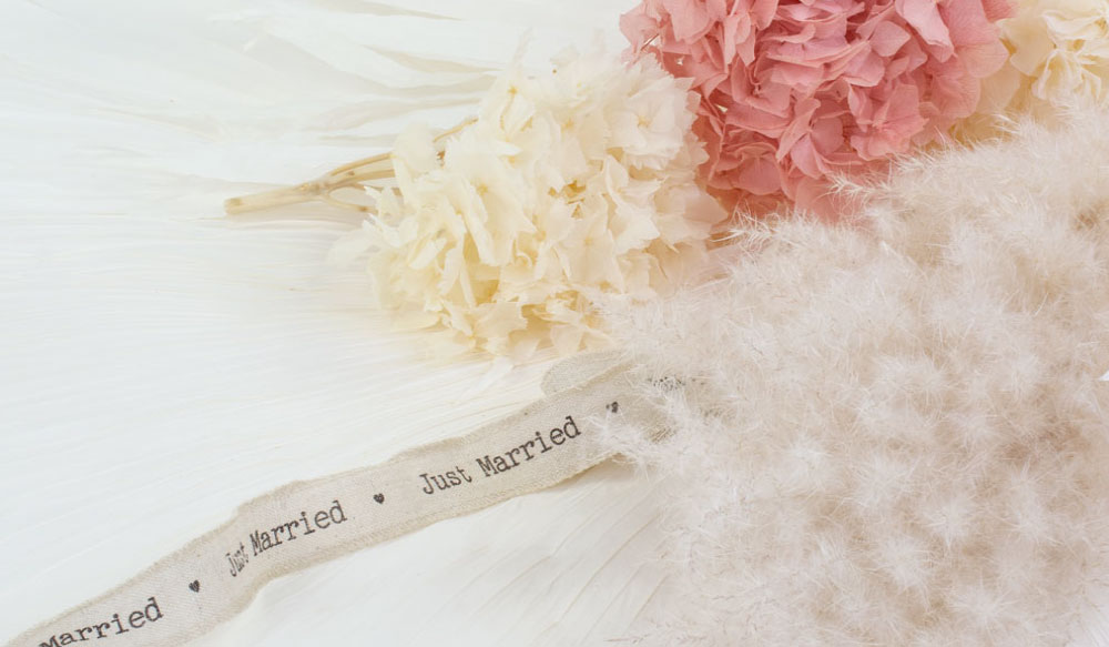 a group of natural white dried pampas grass, white and pink preserved hydrangeas, bright white palmetto palm leaves, and Just Married linen ribbon